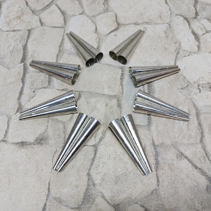 May include: A set of ten silver metal cones, arranged in a star shape on a grey stone surface.