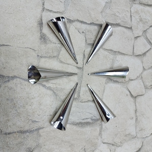 May include: Six silver metal cones arranged in a star shape on a grey textured background. The cones are used for making pastry.