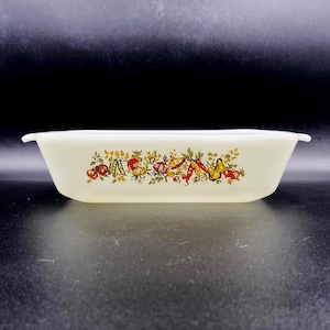 May include: Off-white rectangular casserole dish with a colorful vegetable design. The dish features a border of tomatoes, peppers, and other produce. The dish has two small handles on either side.
