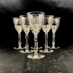 May include: Six clear crystal wine glasses with etched floral designs. The glasses have a stemmed base and a wide bowl. The background is black.