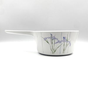 May include: White saucepan with a long handle. The side of the pan features a floral design of purple irises and green stems. The pan is set against a white background.