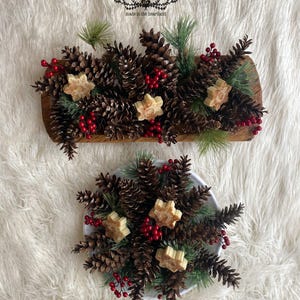 May include: A wooden tray and a white plate filled with pine cones, red berries, and star-shaped soaps. The tray has the text "little box made in the heartland" on it.