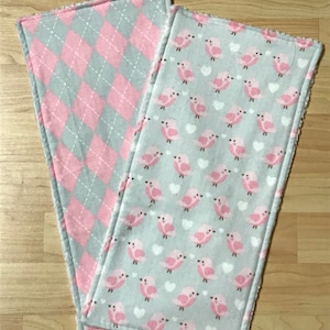 May include: Two gray and pink burp cloths. One cloth has a pink and gray diamond pattern. The other cloth has a pattern of pink birds and white hearts.