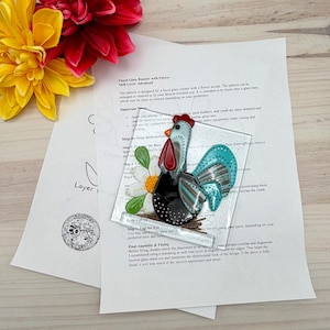 Puede incluir: Gallo de vidrio fusionado con un adorno floral. El gallo presenta una cresta roja, un ala turquesa y un cuerpo negro. Una flor blanca con un centro amarillo está al lado del gallo. La imagen incluye instrucciones y flores.