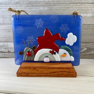 K&ouml;nnte beinhalten: Blaue Weihnachtsdekoration aus Glas mit Rentier, Wichtel und Schneemann. Die Figuren sind rot, wei&szlig; und gr&uuml;n, mit Schneeflocken-Akzenten. Auf einem Holzst&auml;nder montiert, mit einer Juteschnur zum Aufh&auml;ngen.
