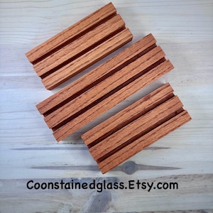 May include: Three wooden soap dishes with a grooved design, made of reddish-brown wood. The dishes are arranged diagonally on a light wood surface. The text "Coonstainedglass.Etsy.com" is visible at the bottom.