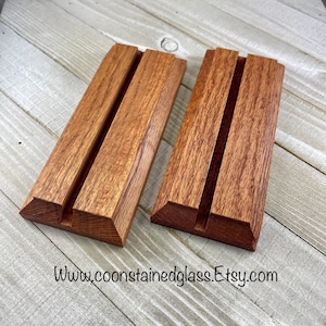 May include: Two wooden display stands with a groove in the center. The stands are made of a reddish-brown wood and have a natural finish.