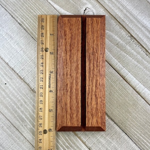 Op de afbeelding: Een rechthoekige houten telefoonhouder met een verticale sleuf, ongeveer 15 cm hoog. De houder is gemaakt van roodbruin hout met een zichtbaar nerfpatroon. Een liniaal is naast de houder geplaatst voor de schaal.
