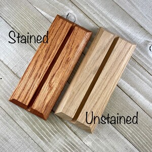 K&ouml;nnte beinhalten: Zwei Handyhalter aus Holz, einer in warmem Braun gebeizt und der andere unbehandelt, Naturholz. Jeder St&auml;nder hat eine Nut zur Aufnahme eines Telefons. Das Wort "Stained" steht auf dem linken St&auml;nder und "Unstained" auf dem rechten.