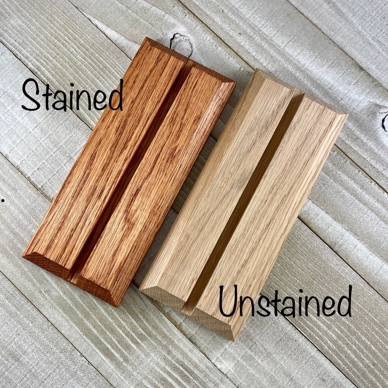 K&ouml;nnte beinhalten: Zwei Handyhalter aus Holz, einer in warmem Braun gebeizt und der andere unbehandelt, Naturholz. Jeder St&auml;nder hat eine Nut zur Aufnahme eines Telefons. Das Wort "Stained" steht auf dem linken St&auml;nder und "Unstained" auf dem rechten.