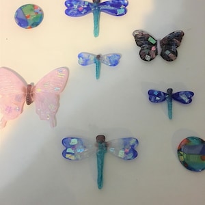 May include: Assortment of colorful glass butterflies and dragonflies. The butterflies are pink, black, and white. The dragonflies are blue, white, and green.