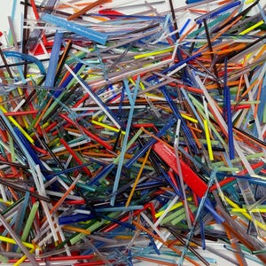 May include: A close-up view of a pile of colorful glass rods. The rods are various lengths and widths, and in shades of red, blue, green, yellow, and clear. The rods are scattered and overlapping, creating a textured and abstract design.