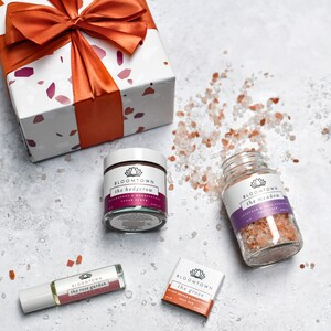 Puede incluir: Tres frascos de vidrio con exfoliantes de sal rosa del Himalaya. Los frascos est&aacute;n etiquetados con 'Bloomtown' y tienen diferentes aromas: 'The Hedgerow', 'The Meadow' y 'The Grove'. Los frascos est&aacute;n sobre una superficie blanca con una caja de regalo en el fondo.
