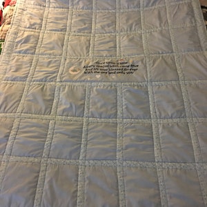 May include: A light blue baby quilt with a white and blue polka dot pattern. The quilt is quilted in a grid pattern and has a personalized embroidered message that reads "Once upon a time Avery special wish came true And life was blessed forever With the one and only you".