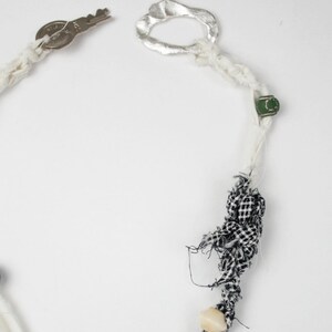 May include: A white and black fabric necklace with a silver pendant featuring a stylized animal design. The necklace also includes a key, a silver ring, and several colorful beads.