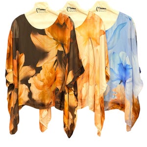 May include: Three sheer tops with floral prints in brown, orange, and blue, displayed on neutral hangers. The tops feature a loose, flowing design, a scoop neckline, and a tie at the hem. The floral pattern is large and striking.