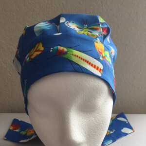 Puede incluir:  gorro de quirófano azul con estampado de mariposas y libélulas de colores. El gorro tiene una corbata que se puede atar en la parte posterior del cuello.