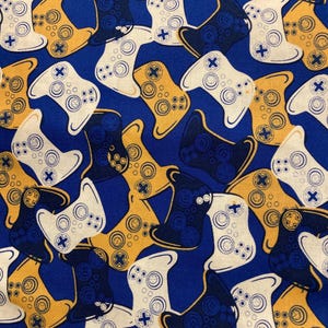 May include: A fabric with a repeating pattern of video game controllers in white, gold, and navy blue on a blue background. The controllers have buttons and directional pads.