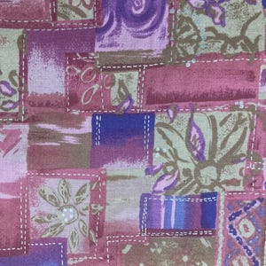 May include: Close-up of a patchwork fabric with a mix of colors including pink, purple, and tan. The design features rectangular and square shapes with floral and abstract patterns, stitched together with white thread.