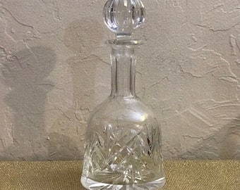 May include: A clear glass decanter with a cut crystal design and a round stopper. The decanter has a wide base and a narrow neck.