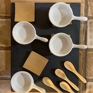 May include: A set of four white ceramic ramekins with handles, four wooden spoons, and four square wooden coasters on a black slate serving tray with a wooden frame.