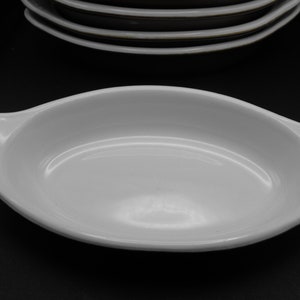 May include: White oval baking dish with two handles. The dish is made of ceramic and has a smooth, glossy finish.