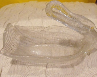May include: A clear glass swan-shaped dish with a textured surface. The dish is designed to hold small items like jewelry or trinkets.