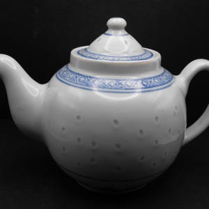 May include: A white teapot with a blue and white patterned design. The teapot has a round body and a lid with a small hole in the top.