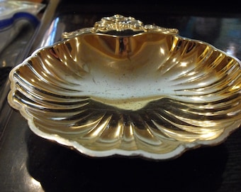 Könnte beinhalten: Eine goldfarbene Metallschale in Form einer Muschel mit einem dekorativen Blumendesign am Griff.