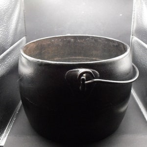 May include: A black cast iron pot with a single handle and a hinged lid. The pot is empty and has a rustic appearance.