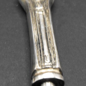 May include: A silver pen with a detailed, textured design on the barrel and a pointed tip.