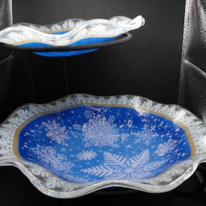 May include: Two blue glass serving bowls with a white snowflake design. The bowls are on a metal stand.