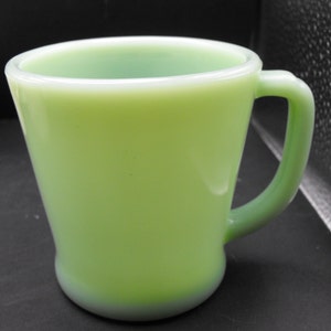 Puede incluir: Una taza de cerámica de color verde pálido con forma redondeada y asa. La taza está hecha de un material liso y opaco.