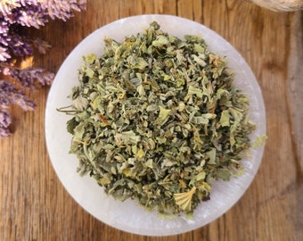 May include: A white bowl filled with dried green herbs. The bowl is sitting on a wooden surface.