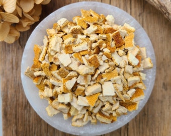 May include: A white bowl filled with dried orange peel pieces. The peel is a light orange color and has a slightly rough texture.