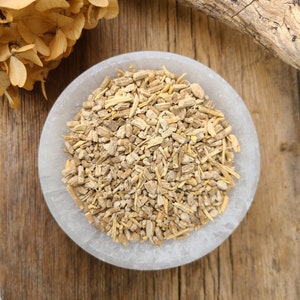 May include: A white bowl filled with dried, light brown, and beige root pieces. The bowl is sitting on a wooden surface.