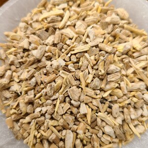 May include: A close-up view of a bowl filled with dried, light brown, and beige root pieces. The root pieces are irregularly shaped and have a rough texture.