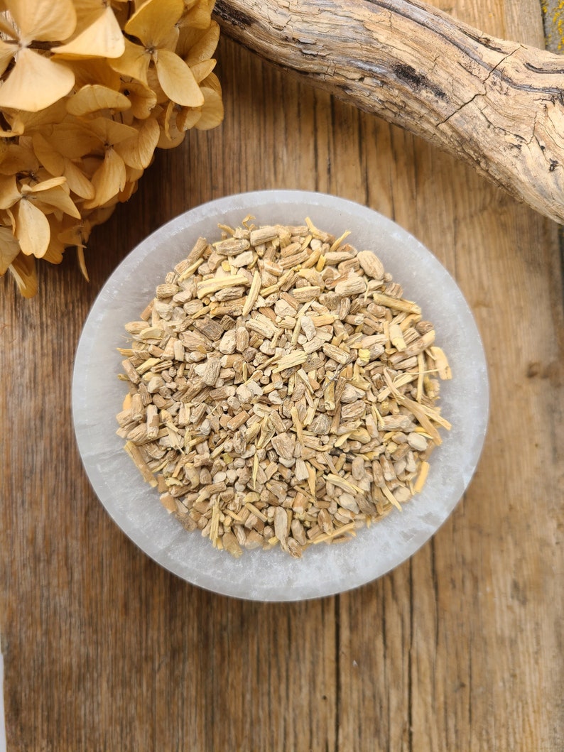 May include: A white bowl filled with dried, light brown, and beige root pieces. The bowl is sitting on a wooden surface.