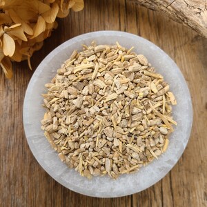 May include: A white ceramic bowl filled with dried, light brown, and beige root pieces. The bowl is sitting on a wooden surface.