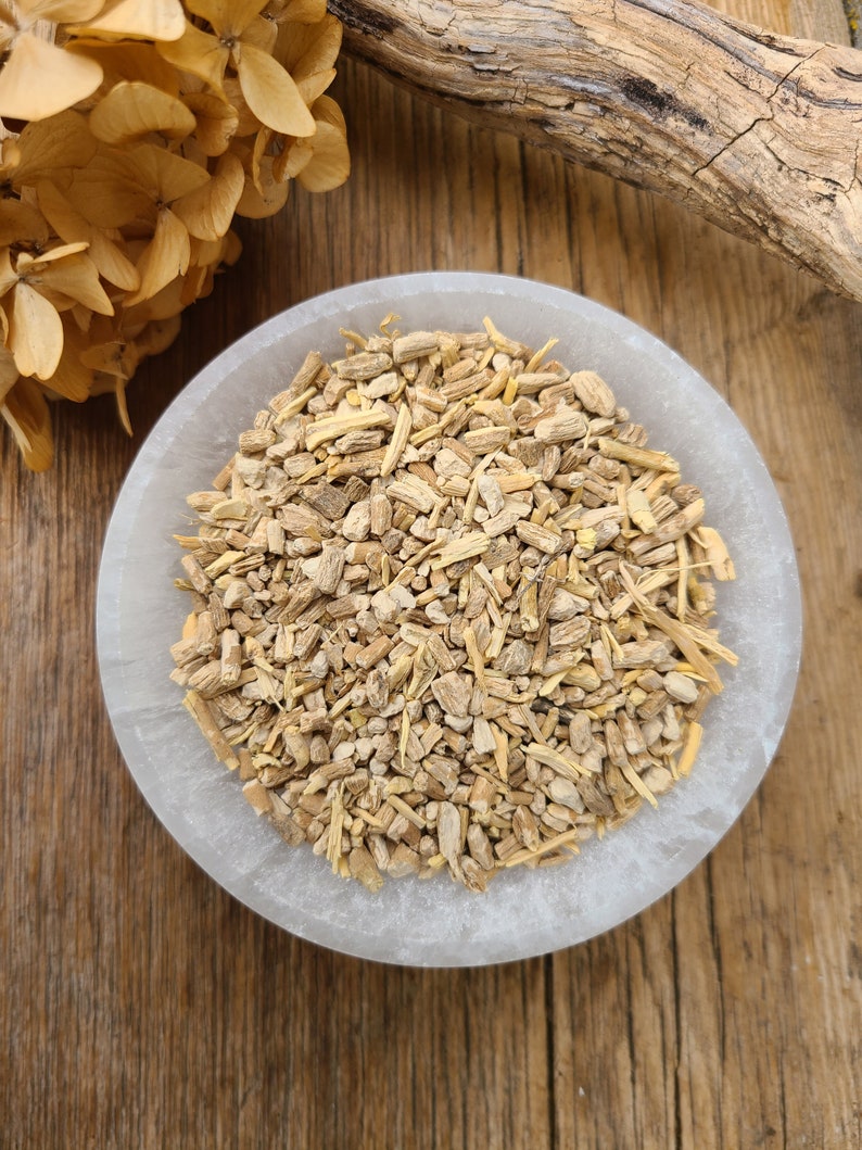 May include: A white ceramic bowl filled with dried, light brown, and beige root pieces. The bowl is sitting on a wooden surface.