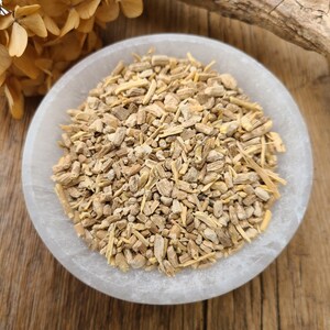 May include: A white bowl filled with dried, light brown, and beige root pieces. The bowl is sitting on a wooden surface.