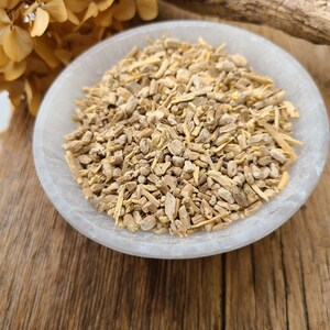 May include: A white bowl filled with dried, light brown, and beige root pieces. The bowl is sitting on a wooden surface.