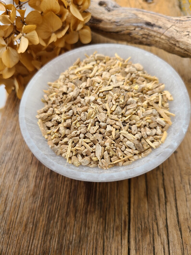 May include: A white bowl filled with dried, light brown, and beige root pieces. The bowl is sitting on a wooden surface.