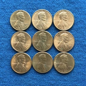 May include: Nine copper-colored 1989 Lincoln pennies arranged in a grid pattern. Each coin features a profile of Abraham Lincoln, the word "LIBERTY," and the phrase "IN GOD WE TRUST."