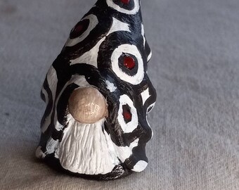 May include: A small gnome figurine with a white beard and a black and white hat with red circles. The gnome is painted in a geometric pattern.