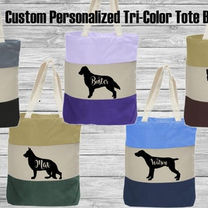 May include: Five custom tote bags with different dog silhouettes and names. Each bag is made of three colors of canvas fabric. The bags are arranged in a row on a woodgrain background.