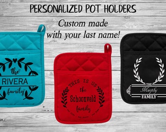 May include: Three personalized pot holders with different last names and designs. The pot holders are red, blue, and black. The designs include a wreath with the family name, a wreath with the text "This is us, the [last name] family", and a wreath with the text "The [last name] family".