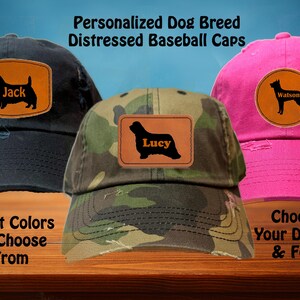 Peut inclure: Trois casquettes de baseball usées avec des silhouettes de races de chiens personnalisées et des noms. Les casquettes sont noires, camouflage et roses. Le texte sur les casquettes indique "Jack", "Lucy" et "Watson".