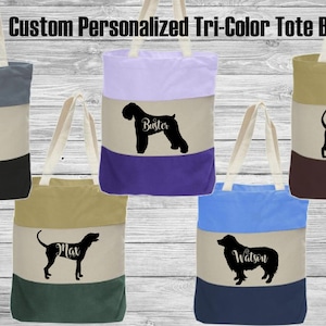 May include: Five personalized tri-color tote bags with different dog breeds and names. The bags are made of canvas and have a natural cotton handle. The bags are in the following colors: gray, black, beige, purple, beige, blue, beige, navy. The dog breeds are: Black and Tan Coonhound, Black Russian Terrier, Black and Tan Coonhound, Australian Shepherd.