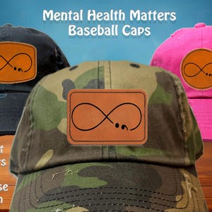 May include: Baseball caps in various colors, including black, camouflage, and pink, are displayed. Each cap features a leather patch with a black infinity symbol design. The text "Mental Health Matters Baseball Caps" is visible.